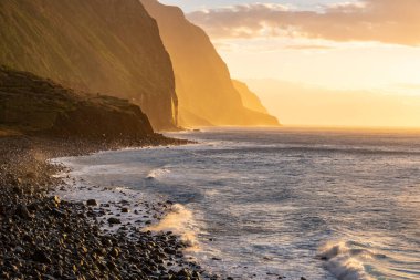Volkanik kaya kayalıkları güneş ışığında Achadas da Cruz. Atlantik Okyanusu dalgaları. Portekiz, Madeira tatil köyünün güzel gün batımı deniz manzarası