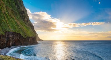 Volkanik kaya kayalıkları güneş ışığında Achadas da Cruz. Atlantik Okyanusu dalgaları. Portekiz, Madeira tatil köyünün güzel gün batımı deniz manzarası