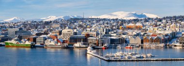 Kışın Norveç 'in Tromso şehrinin panoraması. Karlı çatılar, liman ve balıkçı tekneleri yakınındaki set, güneşli kış günü..