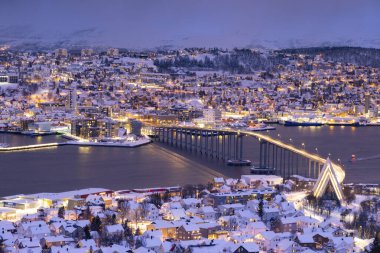 Kışın Norveç 'in Trom şehrinin Panorama' sı. Karlı çatılar, köprü, liman ve balıkçı gemilerinin yakınındaki set. Akşam ışıkları