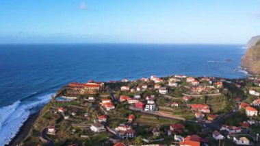 Madeira adasının havadan 4k 'lık günbatımı görüntüsü. Gökkuşağı, muz tarlaları, küçük otelleri olan turist köyü. Deniz manzaralı güzel sahil kasabasının güzellikleri.