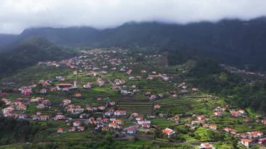 Sao Vicente, Madeira Adası, Portekiz 'in geleneksel teras köyünün havası. Fırtınalı havada yeşil bir dağ manzarası arasında küçük evler ve bahçeler.