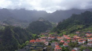 Sao Vicente, Madeira Adası, Portekiz 'in geleneksel teras köyünün havası. Fırtınalı havada yeşil bir dağ manzarası arasında küçük evler ve bahçeler.