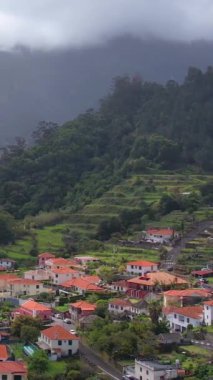 Sao Vicente, Madeira Adası, Portekiz 'in geleneksel teras köyünün havası. Fırtınalı havada yeşil bir dağ manzarası arasında küçük evler ve bahçeler.