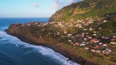 Madeira adasının havadan 4k 'lık günbatımı görüntüsü. Gökkuşağı, muz tarlaları, küçük otelleri olan turist köyü. Deniz manzaralı güzel sahil kasabasının güzellikleri.