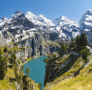 Oeschinensee lake with snow Bluemlisalp mountain on sunny summer day. Panorama of the azure lake Oeschinensee, pine forest in Swiss alps, Kandersteg. Switzerland. clipart