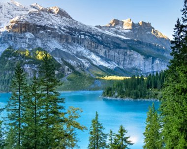 Idyllic morning view of the lake Oeschinensee. Location Swiss alps, Switzerland, Kandersteg district. Blue mountain lake with pine trees and mountains in background. clipart