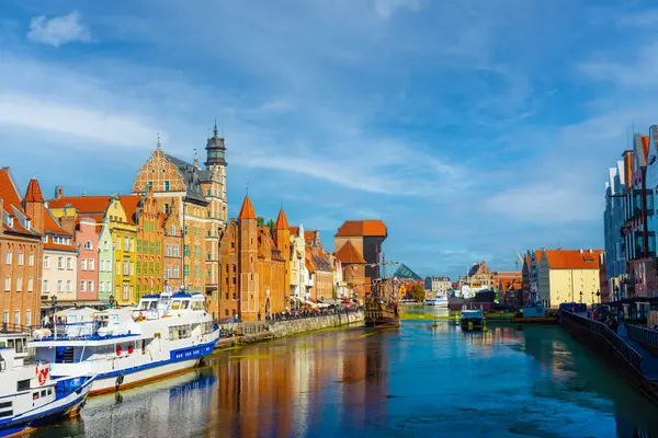 Polonya 'nın Gdansk kentindeki tarihi renkli binaların yanında Motlawa Nehri' nden geçen iki teknenin manzarası. Parlak mavi gökyüzü bu canlı Avrupa şehir manzarasını güçlendirir