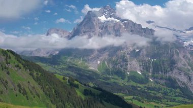 Sinema insansız hava aracı Grindelwald 'ın nefes kesici manzarası üzerinde uçuyor. Etrafı yüksek dağ zirveleri ve yemyeşil vadilerle çevrili. Kar tepeli zirveler ve dağınık bulutlar. Seyahat ve sağlıklı yaşam tarzı