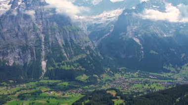 Sinema insansız hava aracı Grindelwald 'ın nefes kesici manzarası üzerinde uçuyor. Etrafı yüksek dağ zirveleri ve yemyeşil vadilerle çevrili. Kar tepeli zirveler ve dağınık bulutlar. Seyahat ve sağlıklı yaşam tarzı