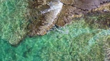 4k Aerial üst turkuaz deniz dalgaları uçurumda kırılıyor. Küçük sıcak dalgalar, sakinlik ve rahatlama. Açık mavi su.