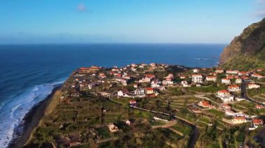 Madeira adasının havadan 4k 'lık günbatımı görüntüsü. Gökkuşağı, muz tarlaları, küçük otelleri olan turist köyü. Deniz manzaralı güzel sahil kasabasının güzellikleri.