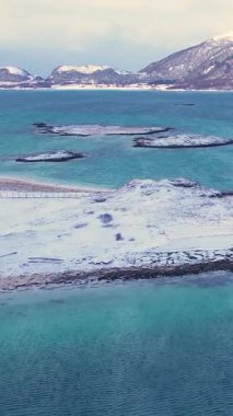 Norveç 'in Sommaroy adasında, güneşli kış mevsiminde, karla kaplı dağ zeminli bir kumsal çevresindeki hava manzarası