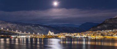 Norveç 'in Tromso şehrinin Panorama' sı Noel mevsiminde bir kış akşamıdır. Fiyort üzerindeki köprü ve evler şehir ışıklarıyla aydınlatılır.