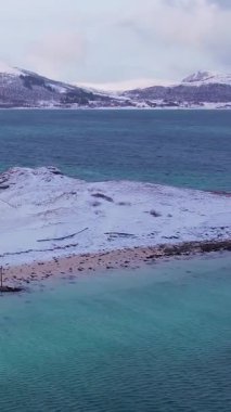 Norveç 'in Sommaroy adasında, güneşli kış mevsiminde, karla kaplı dağ zeminli bir kumsal çevresindeki hava manzarası