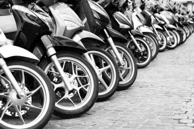 Birkaç motosiklet ve scooter kaldırımlı bir caddede dizilmiş.