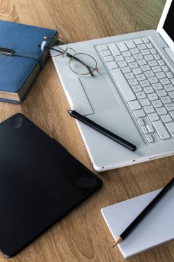 Masadaki dizüstü bilgisayar, defter, kalem ve gözlük.