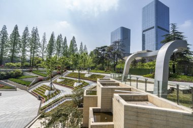 Bahçeli modern bir şehir meydanı. Arka planda katmanlı bahçeleri ve gökdelenleri olan park 