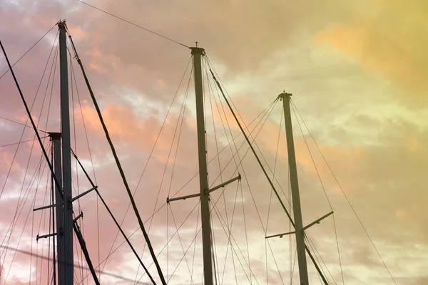 masts of a yacht without sails against the background of a sunset cloudy sky, toned photo