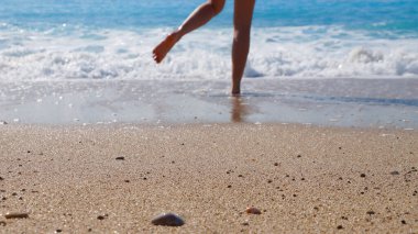 bare feet of a girl run on wet sand to the sea.