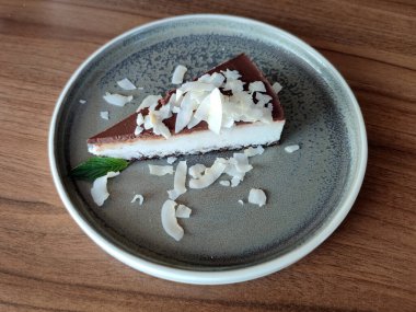 a piece of coconut cheesecake with chocolate icing on a plate close-up