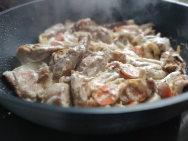 meat with vegetables in cream is fried in a pan close-up