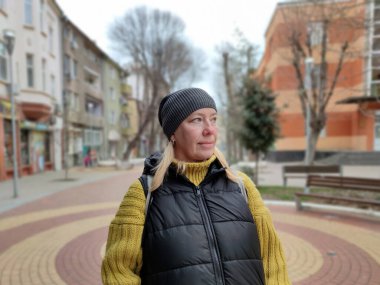 Portrait of a smiling middle-aged blonde woman in a hat on a city street.