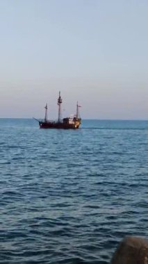 Pleasure tourist ship with a pirate flag sails on the sea, vertical video