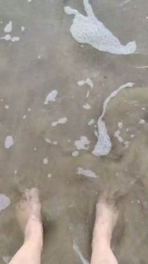 Bare female feet on the sand are washed by the incoming sea wave, top view