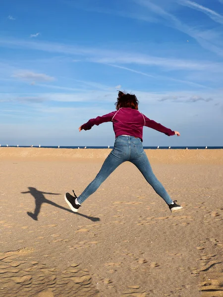 stock image red-haired teen girl jumping with her arms and legs outstretched, rear view.