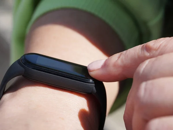 Using a fitness bracelet, a woman presses her finger on the display of a fitness bracelet close-up