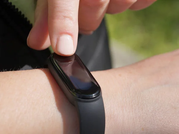 Using a fitness bracelet, a woman measures her pulse on the display of a fitness bracelet close-up