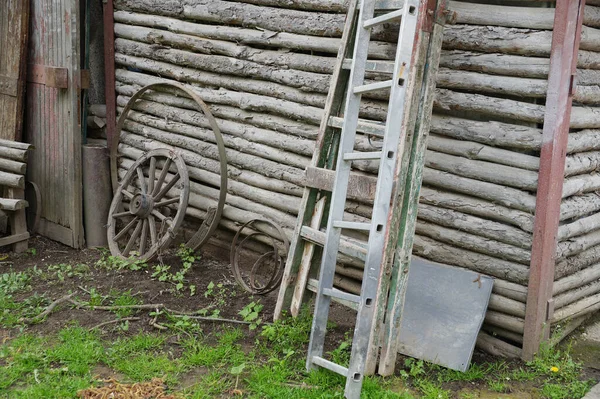 A cart wheel, a wooden ladder against the wall of an old log village house, rural life
