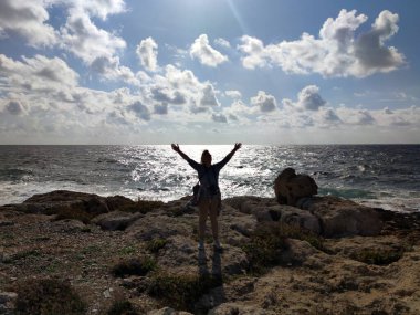 Neşeli kadın kollarını açmış deniz kıyısında duruyor..