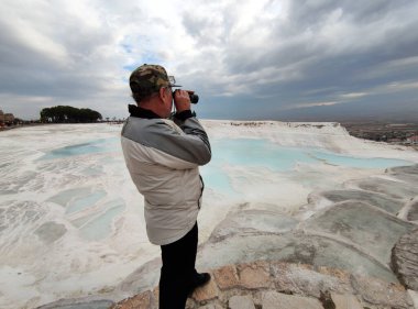 A man looking through a spotting scope from above at the panorama of Pamukkale, Turkey. clipart