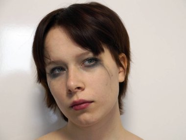 Kısa kahverengi saçları ve maskara bulaşmış gözyaşı lekeli gözleri olan üzgün genç kız..