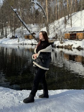 Kışın göl kıyısında beyaz kürklü siyah ceketli gülümseyen kız..