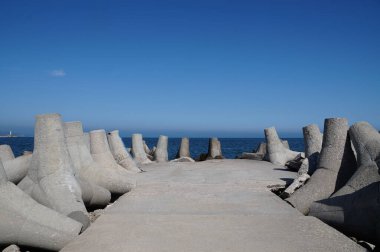 Açık gökyüzü ve deniz ufkuna karşı bir deniz iskelesinde koruyucu beton tetrapodlar.