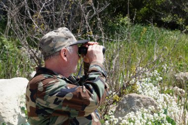 Kamuflaj kıyafetli bir adam doğadaki tek gözlüklü gözlüğe bakar. Yan görünüm.