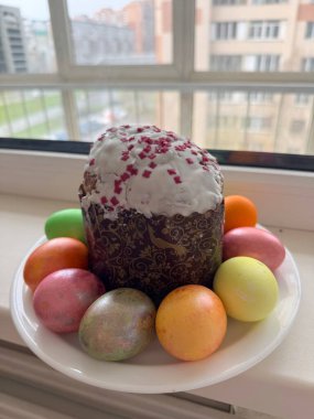 Paskalya pastası şekerli ve beyaz bir tabağa boyanmış yumurtalar pencere kenarında, yakın plan..