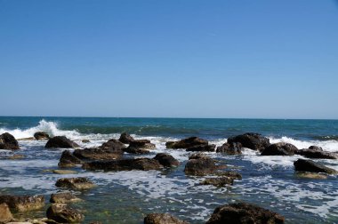 Deniz manzarası, dalgalar suyun kenarındaki büyük kayalara çarpıyor..