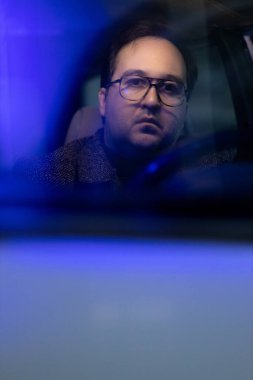 A forty-year-old man in winter clothes and glasses rides in a retro car. He looks thoughtful and tired clipart