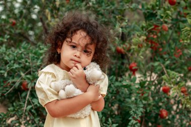Portre. Elinde oyuncakla bej elbiseli kıvırcık saçlı bir kız..