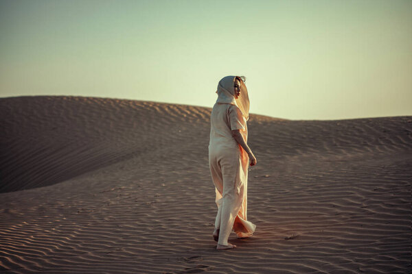 Woman in flowing dress atop desert dune. Golden light, rippled sand. Evokes adventure, solitude, and timeless beauty. Perfect for travel and lifestyle themes.