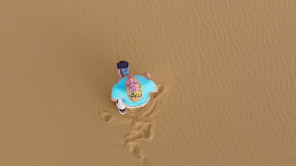 青いセーターの観光客が彼の手で砂漠で彼のドローンをキャッチします 砂丘の上に立つ男の上からの眺め 日没時の航空機運航者 — ストック動画
