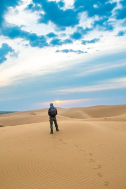 Bir adam gün doğumunda Kyzylkum çölünde bir kum tepesinde duruyor.