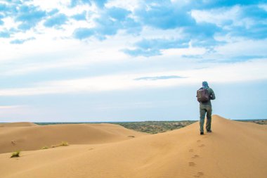 Bir adam gün doğumunda Kyzylkum çölünde bir kum tepesinde duruyor.