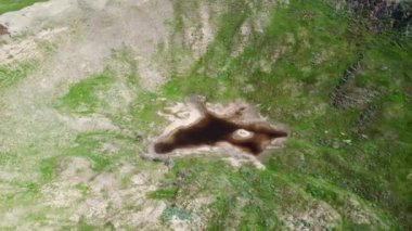 View of the funnel from a nuclear explosion, overgrown with green grass and a lake in the center of the funnel. There are many small craters around the large crater. large meteorite impact crater