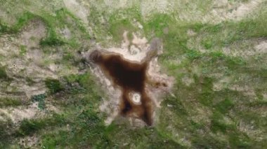 View of the funnel from a nuclear explosion, overgrown with green grass and a lake in the center of the funnel. There are many small craters around the large crater. large meteorite impact crater