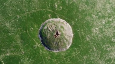 View of the funnel from a nuclear explosion, overgrown with green grass and a lake in the center of the funnel. There are many small craters around the large crater. large meteorite impact crater